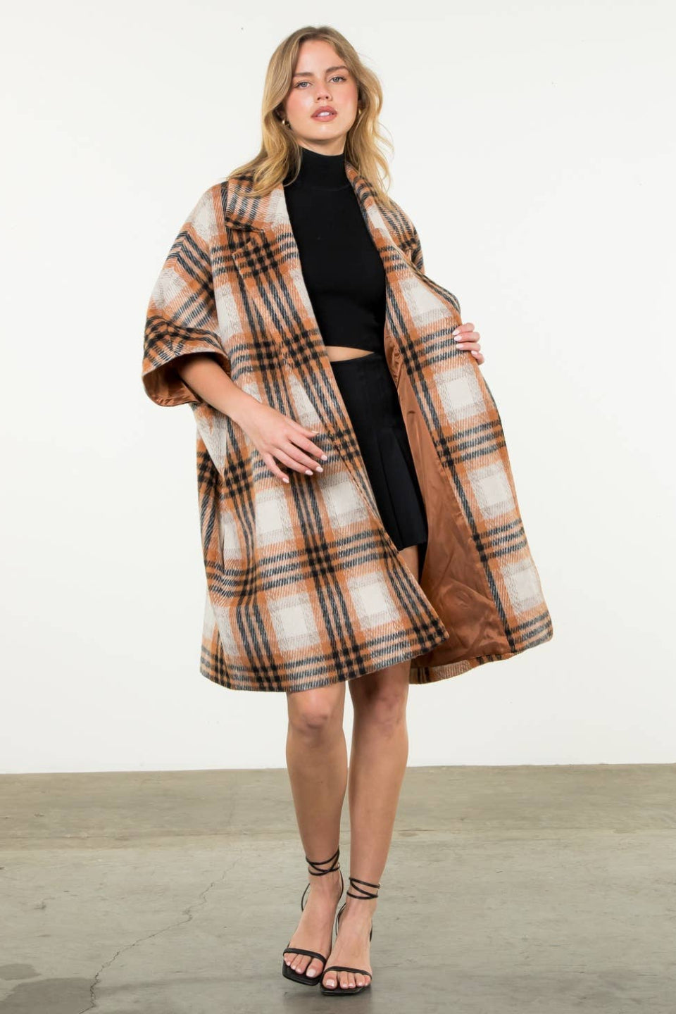 Woman wearing a plaid coat over a black outfit on a white background